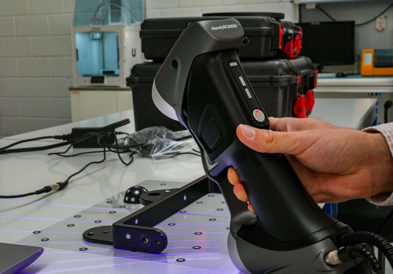 Técnico sosteniendo un escáner 3D HandySCAN, proyectando líneas láser azules sobre un utillaje colocado en una mesa de metrología.
